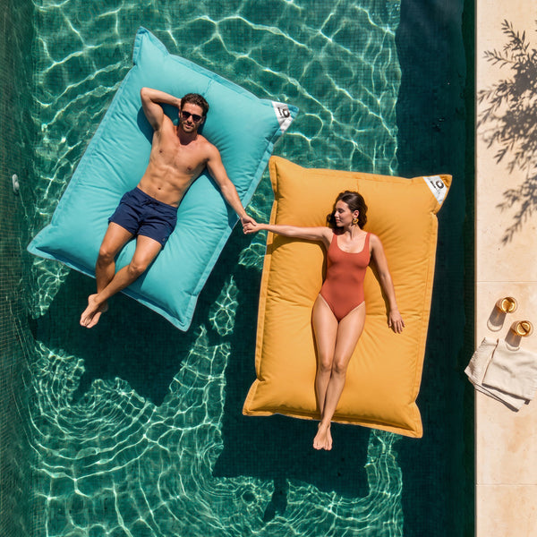 Deux poufs géants flottants Deco Arts, Bleu Caraïbes et Jaune Miel, sur une piscine avec un couple, vue du dessus