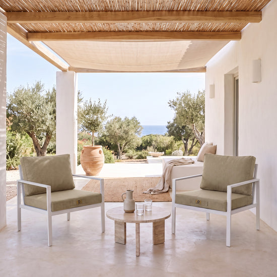 Fauteuilkussens met linnenlook in Beige op twee witte fauteuils onder een overdekte pergola, licht terras uit de zon
