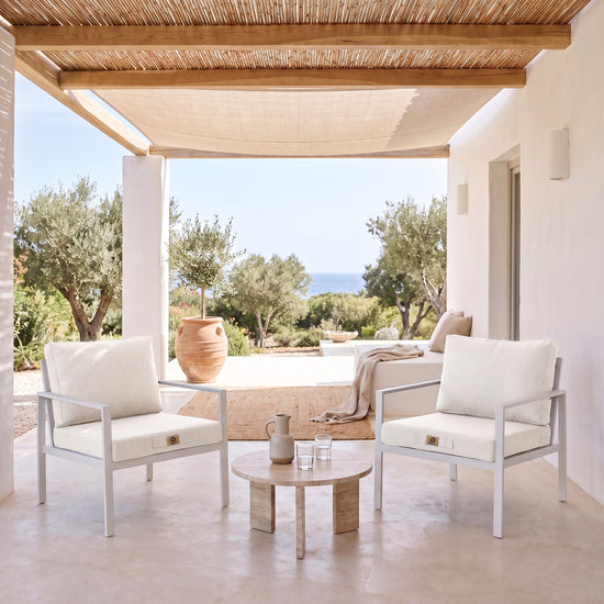 Fauteuilkussens met linnenlook in Gebroken Wit op twee witte fauteuils onder een overdekte pergola, licht terras uit de zon