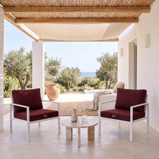 Fauteuilkussens met linnenlook in Pruim op twee witte fauteuils onder een overdekte pergola, licht terras uit de zon