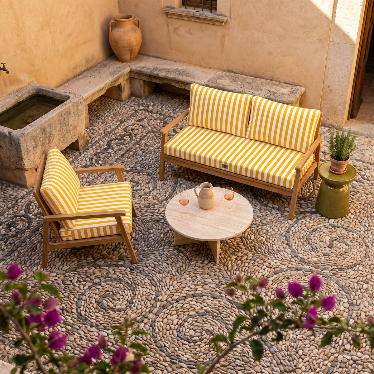 Fauteuil et canapé en teck avec coussins rayés jaune et blanc Deco Arts dans une cour pavée de galets à Majorque