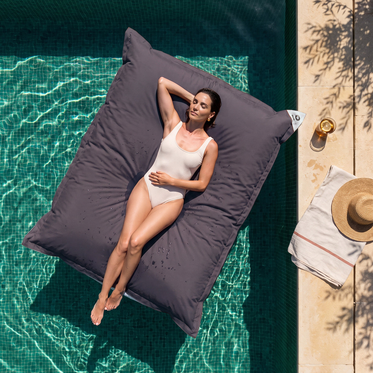 Housse seule à garnir – Pouf géant flottant 180 × 140 cm Gris Carbone sur une piscine, femme allongée au soleil, vue du dessus