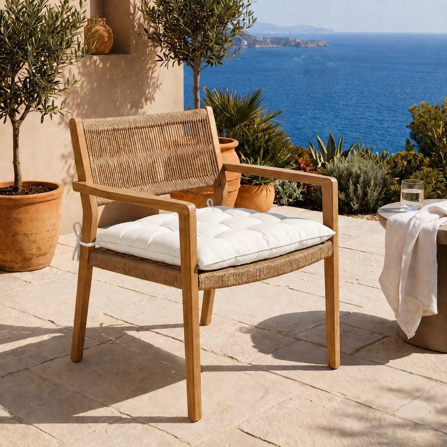 Galette de chaise 40x40 Blanc Cassé sur un fauteuil en bois, terrasse face à la mer